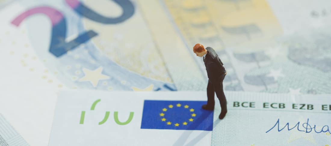 estatuilla en miniatura de un hombre de negocios de pie sobre un billete de cien euros y mirando el símbolo de euro impreso en este