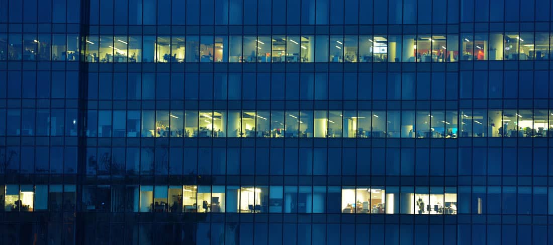 Vista exterior y nocturna de un edificio de oficinas. Solo algunos pisos tienen la luz encendida