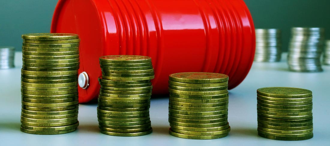 monedas apiladas en cuatro columnas a modo de gráfica y con un barril de petróleo en segundo plano, representa la caída del precio del barril